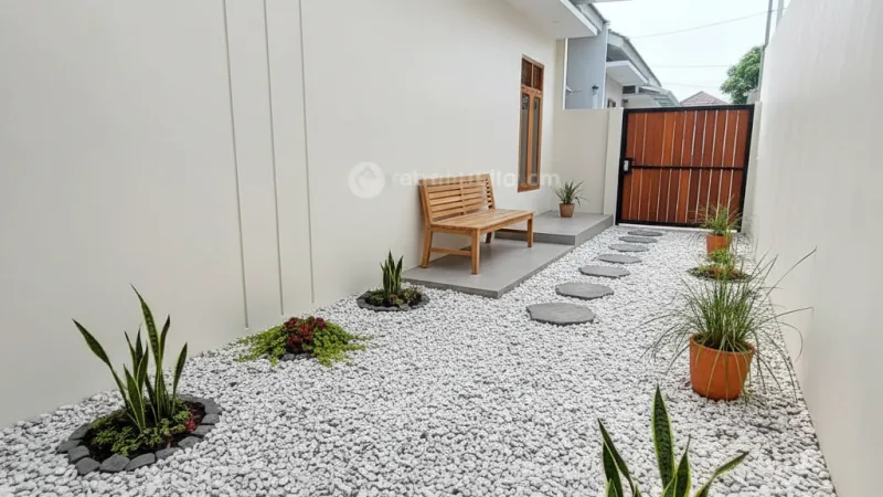 Taman belakang rumah tipe 36 yang didominasi batu koral putih dengan tanaman hias pendek minimalis.